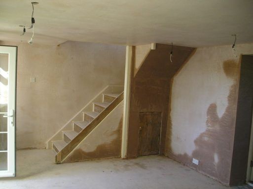 A bare room with a staircase and newly plastered walls.
