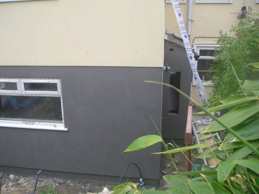 Side of a house with grey-rendered wall and a partially visible window.